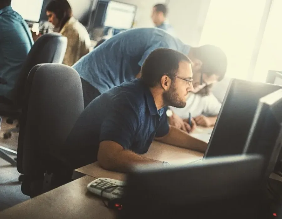 Computer programmer seated at desk in busy office writing code for project